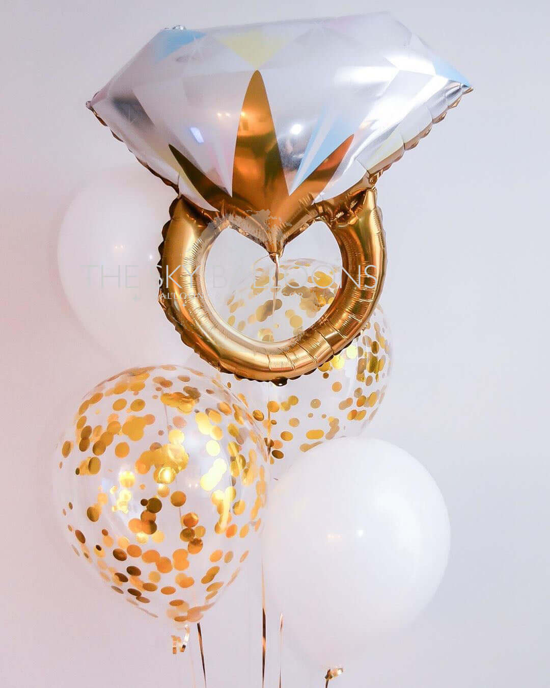 A set of balloons including a latex balloon, a confetti balloon, and a diamond ring balloon, all with a gold and white color scheme and filled with helium gas.