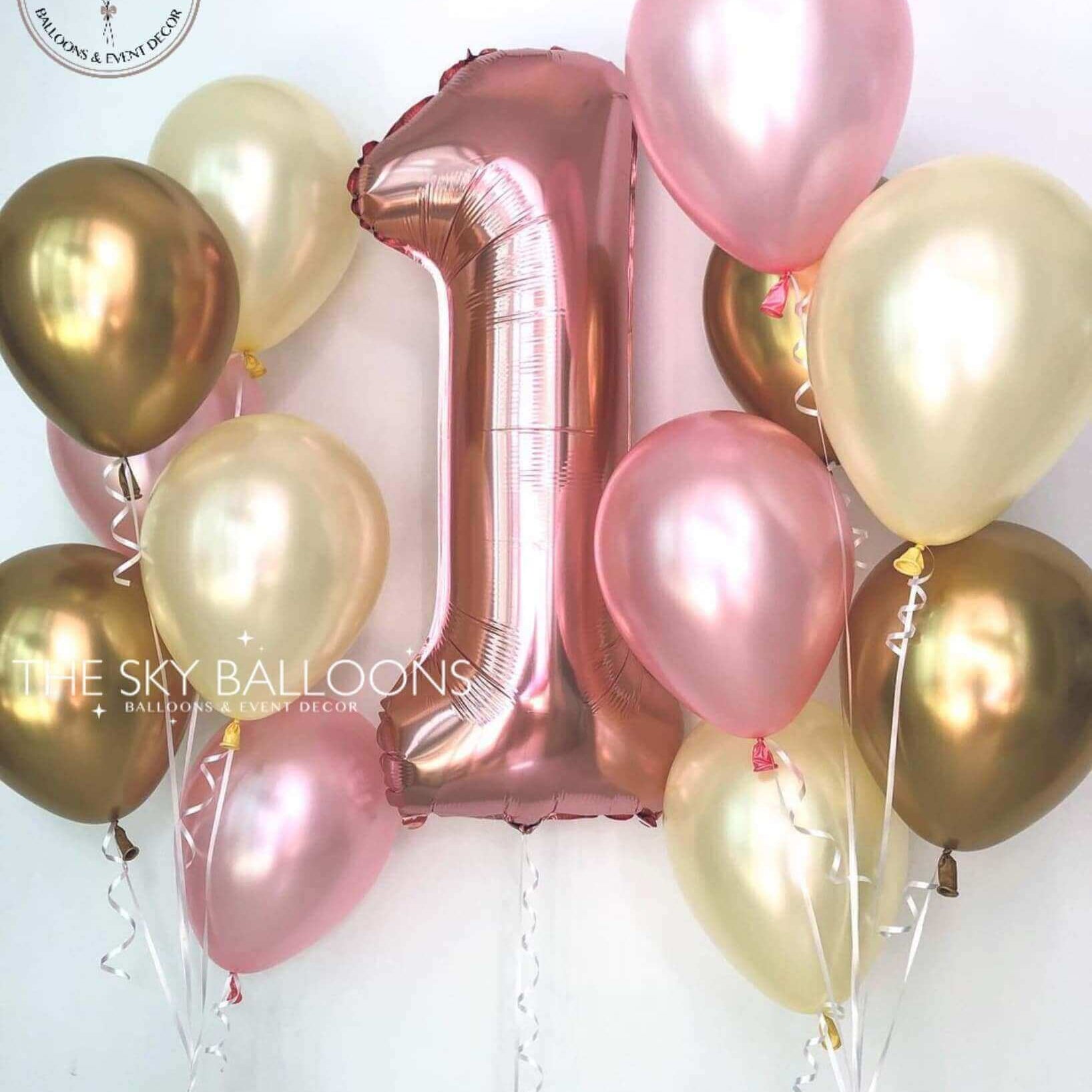 A bouquet of latex balloons in shades of pink and gold, including a large foil number 1 balloon, all tied together with string.