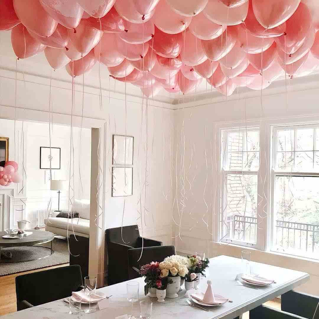 A room with the ceiling decorated with pink pre-inflated balloons creating a festive atmosphere.