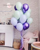 A bouquet of inflated balloons in various shades of purple, green, and white, tied together with a purple ribbon.