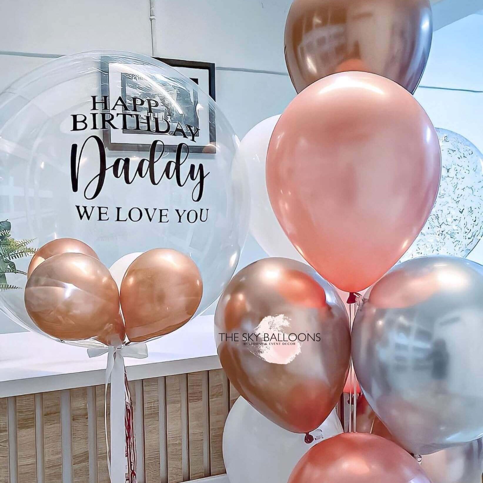 A bouquet of round balloons in shades of pink, silver, and gold, with one balloon featuring a 'Happy Birthday' message and the name 'Daddy', indicating a personalized touch.