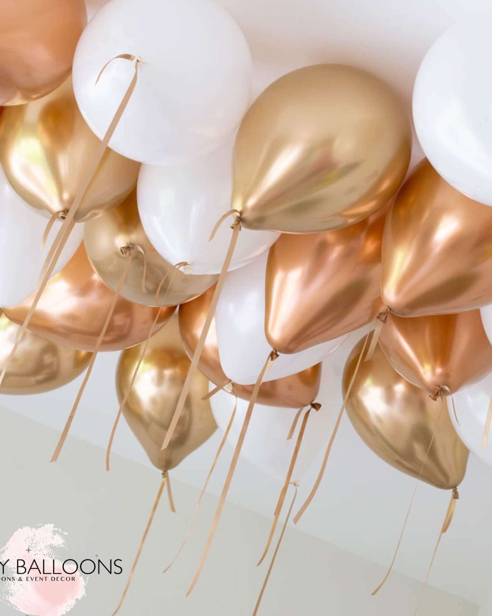 A cluster of helium-filled ceiling balloons in copper, white, and gold colors, tied with strings.