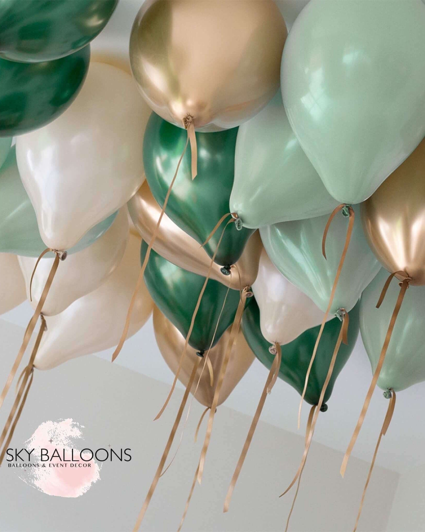 A cluster of helium-filled ceiling balloons in forest green, gold, and white colors, attached to strings.