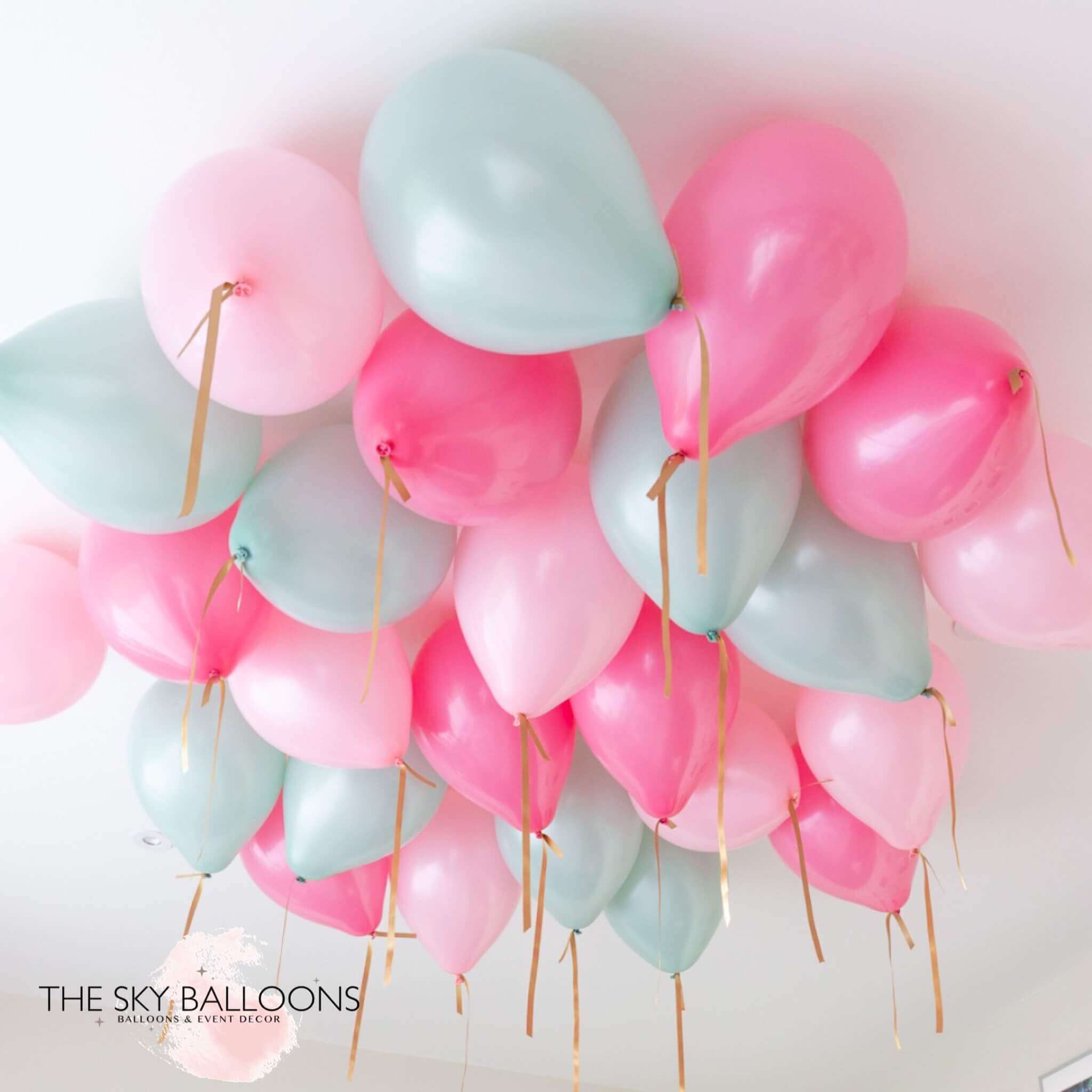 A cluster of round helium balloons in shades of pink and mint green, attached to strings, meant for ceiling decoration.