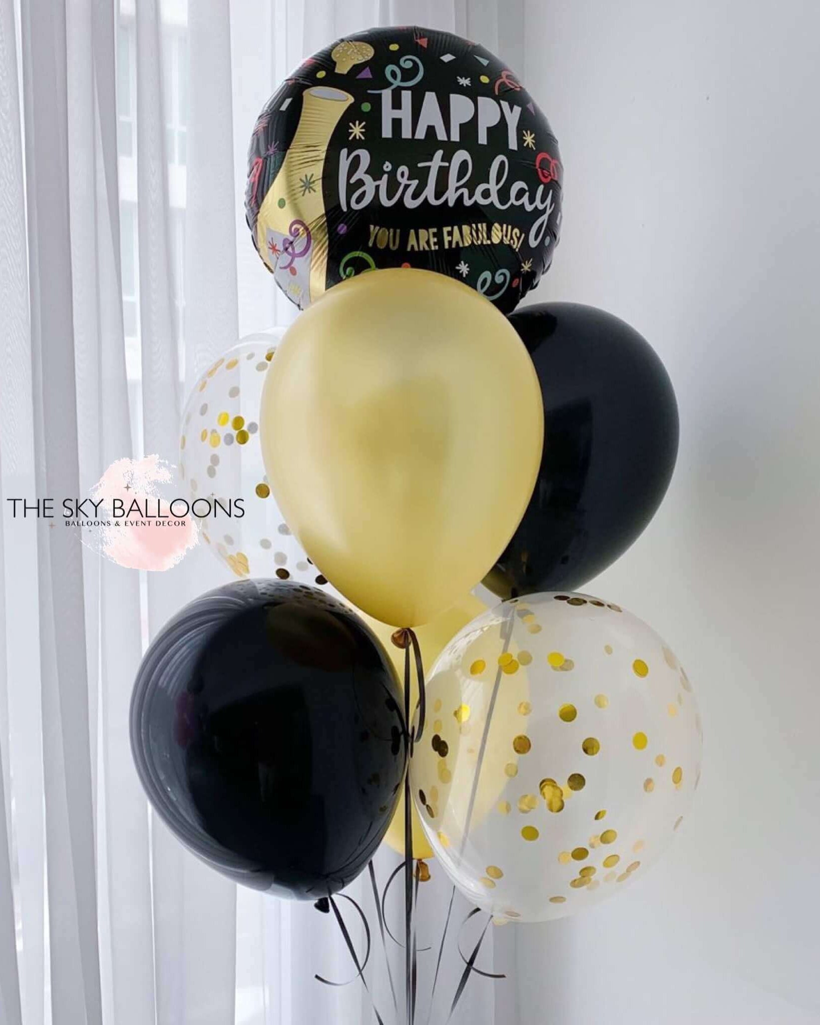 A bouquet of helium-filled birthday balloons in gold, black, and white colors with 'Happy Birthday' and other birthday-related messages printed on them.