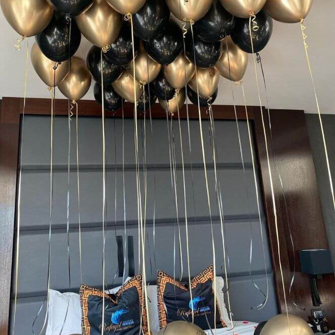 A set of black and gold balloons of various sizes, tied to strings and displayed indoors, likely for a birthday celebration.