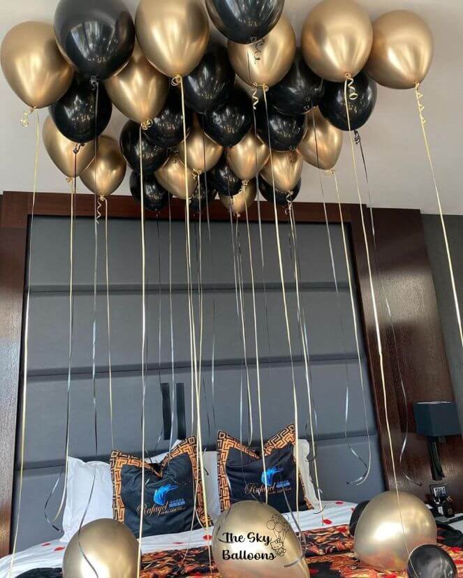 A set of black and gold balloons of various sizes, tied to strings and displayed indoors, likely for a birthday celebration.