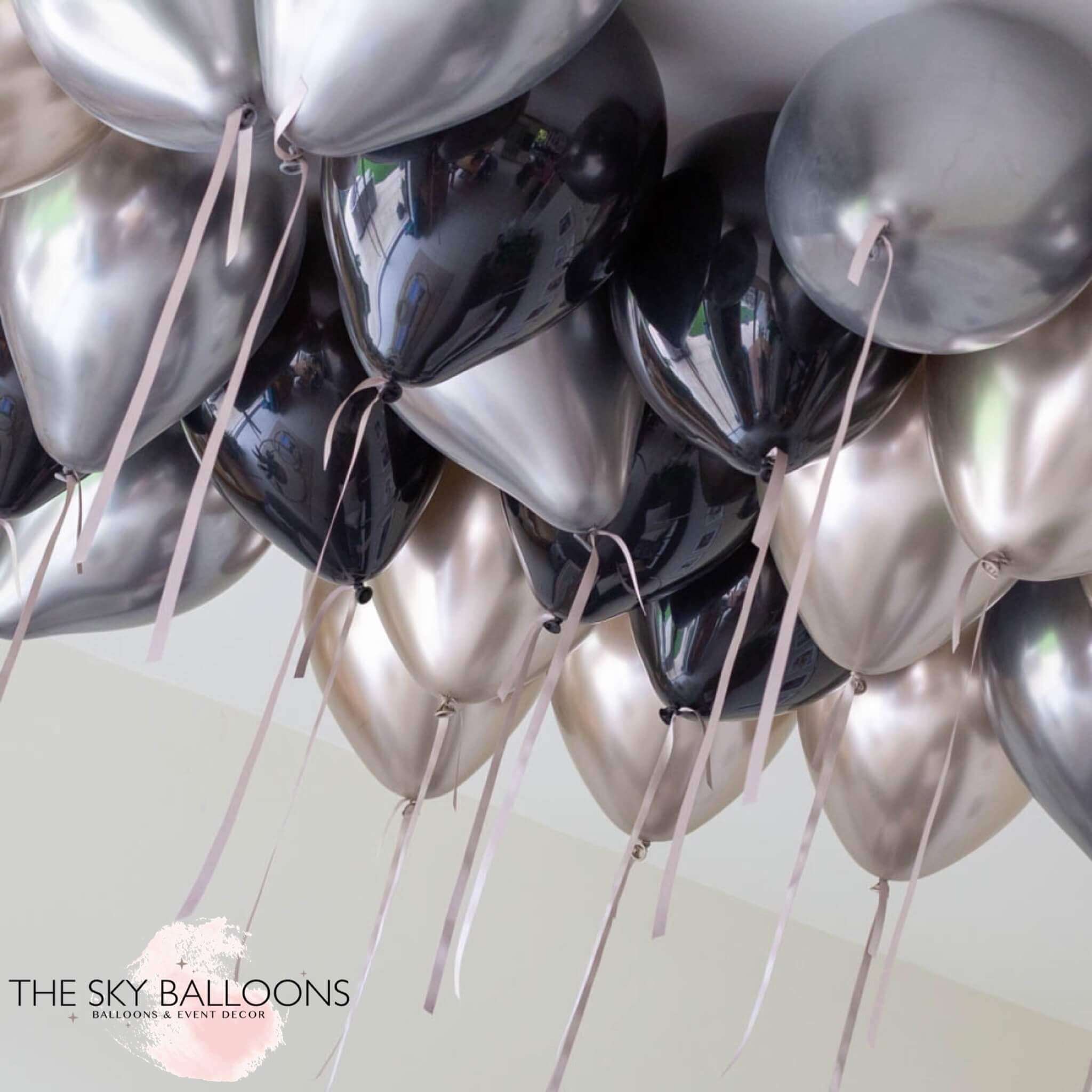 A cluster of inflated round balloons in silver, black, and gold colors, attached to strings, intended for ceiling decoration.