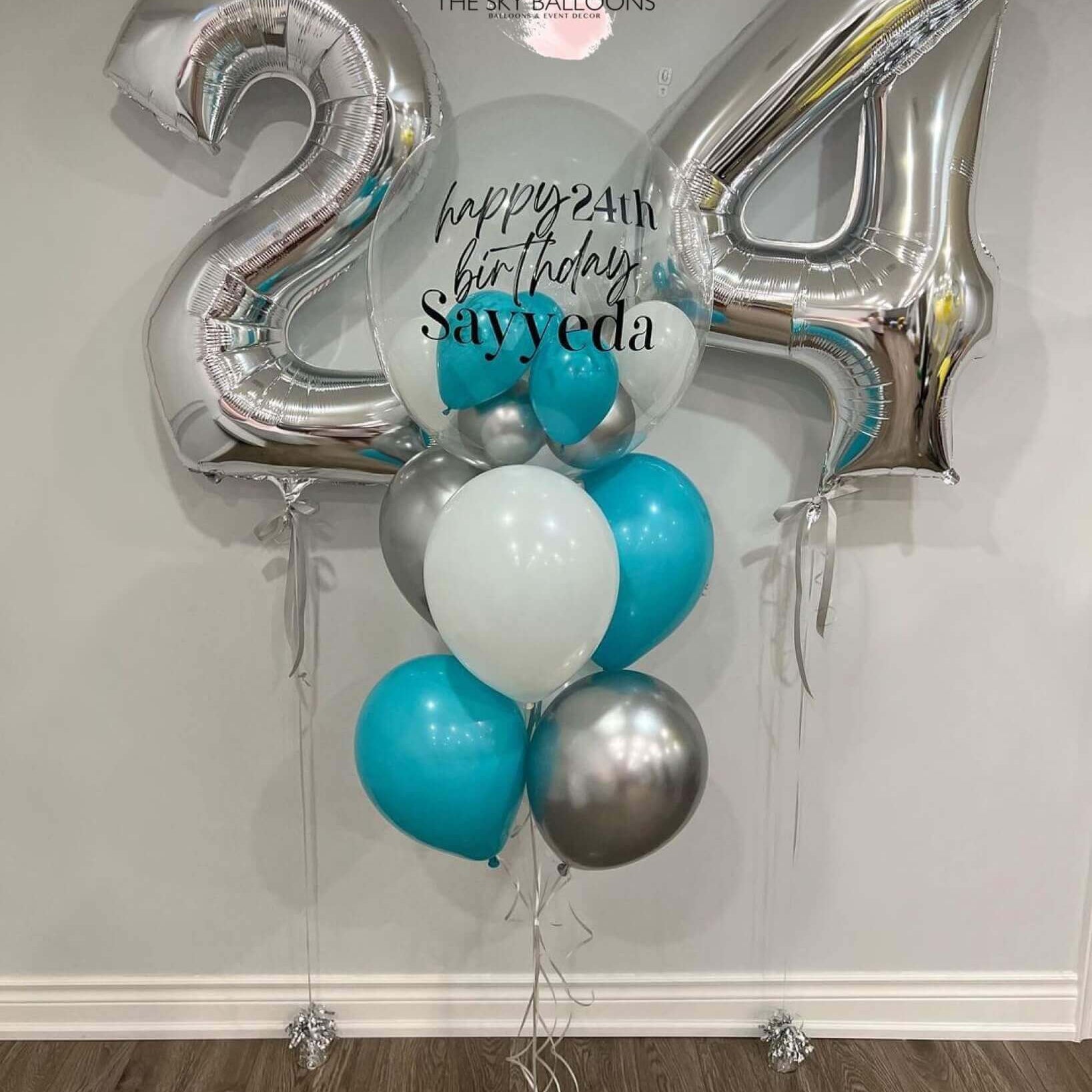A numerical balloon bouquet with the numbers '24' in silver, surrounded by blue and silver balloons, with helium gas, including customized text 'Happy Birthday' and a name 'Sayed'.