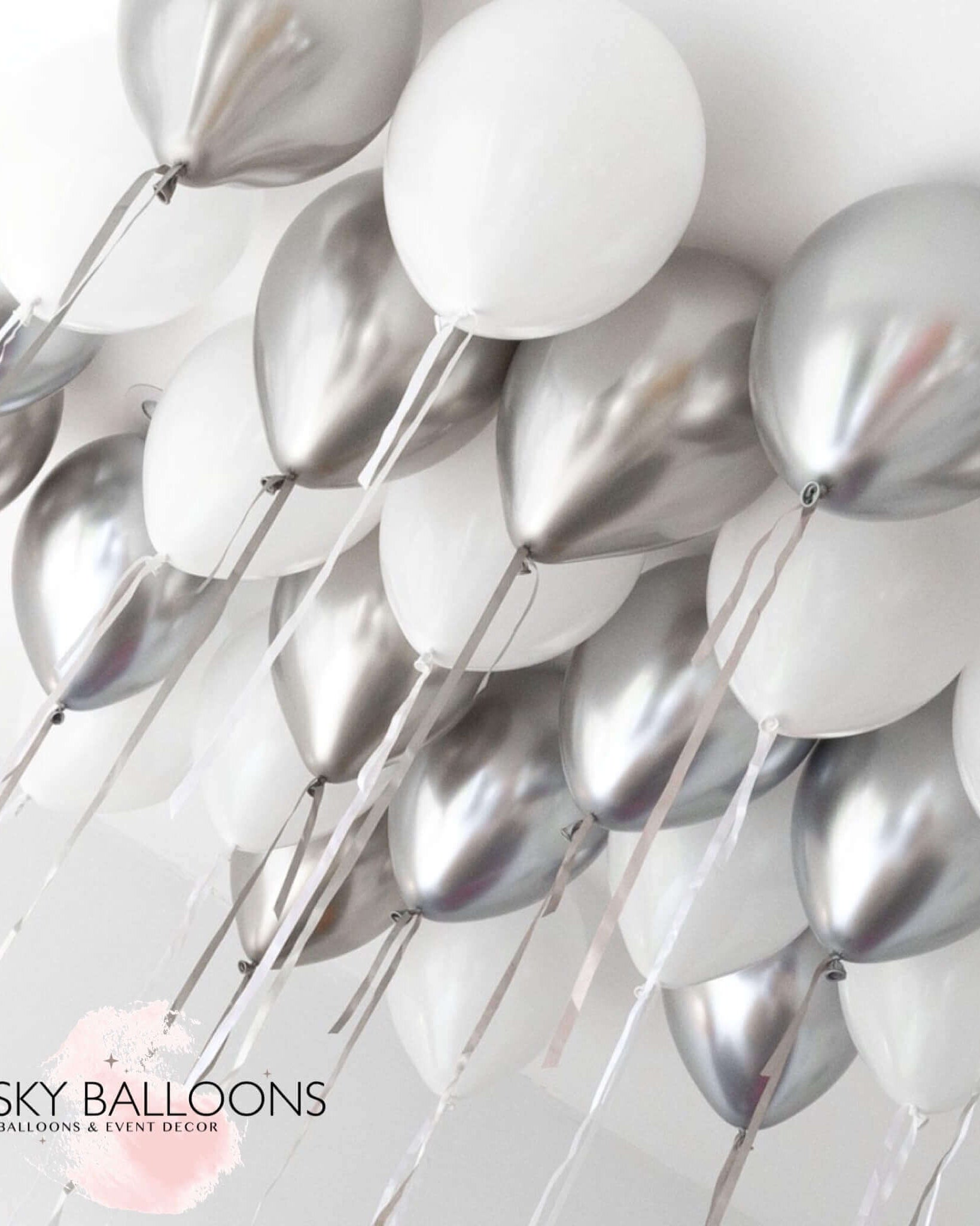 A cluster of inflated helium balloons in white and silver colors, arranged for ceiling decoration.