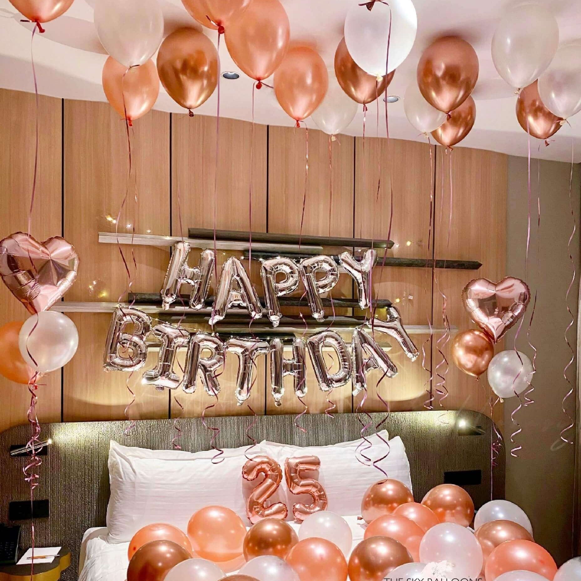 A room decorated with a 'Happy Birthday' banner, balloons in shades of pink and gold, and number foils.