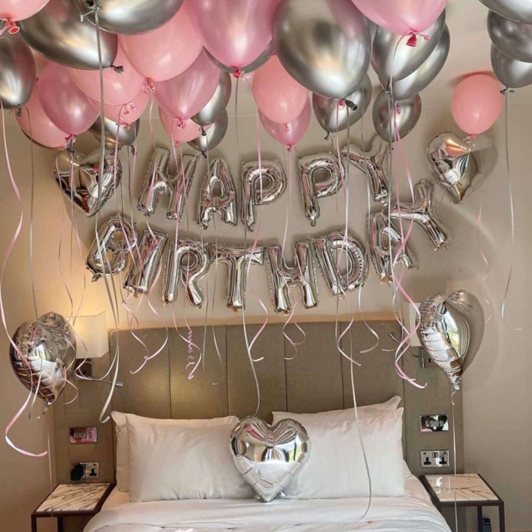 Balloons arranged in a room to spell out 'HAPPY BIRTHDAY' with a heart shape at the end, predominantly in pink and silver colors, celebrating a birthday.