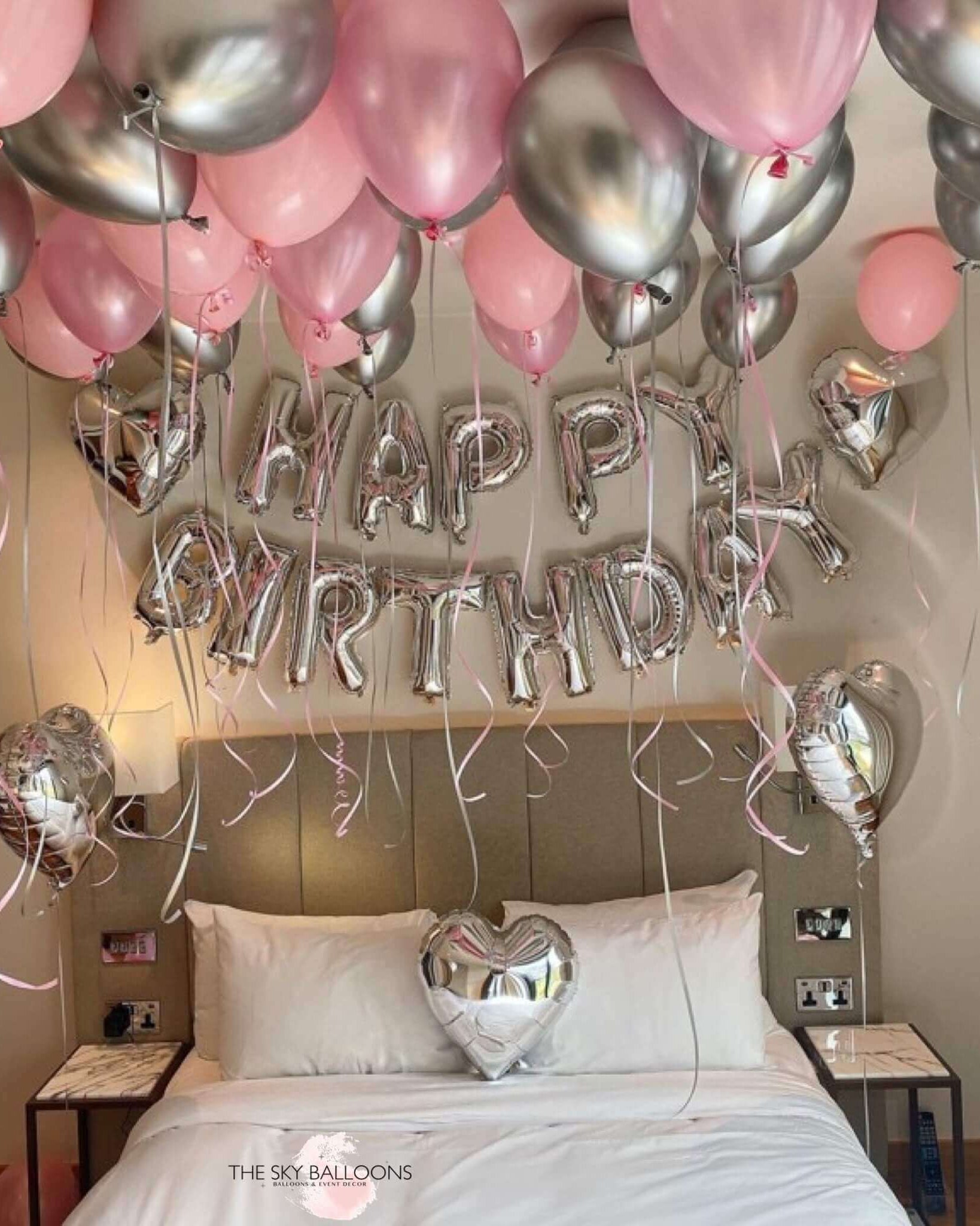 Balloons arranged in a room to spell out 'HAPPY BIRTHDAY' with a heart shape at the end, predominantly in pink and silver colors, celebrating a birthday.
