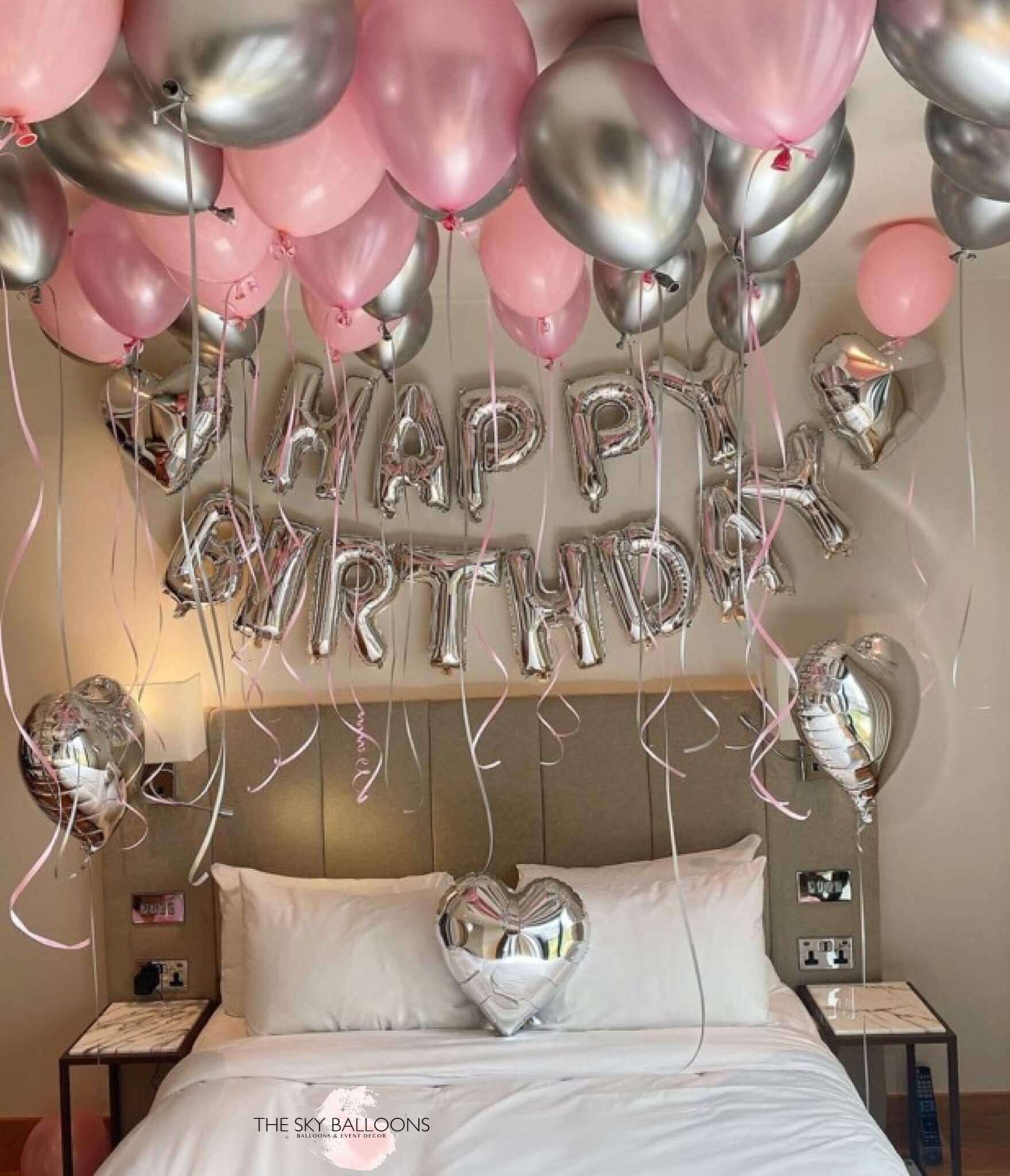 Balloons arranged in a room to spell out 'HAPPY BIRTHDAY' with a heart shape at the end, predominantly in pink and silver colors, celebrating a birthday.