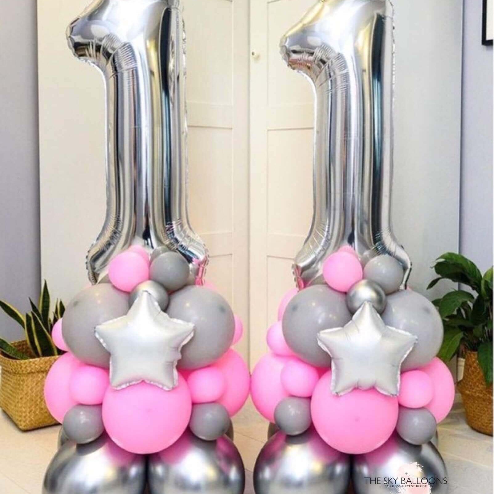 Two balloons designed to form a number, with one balloon in pink and the other in silver, both with star and ball decorations.
