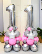 Two balloons designed to form a number, with one balloon in pink and the other in silver, both with star and ball decorations.