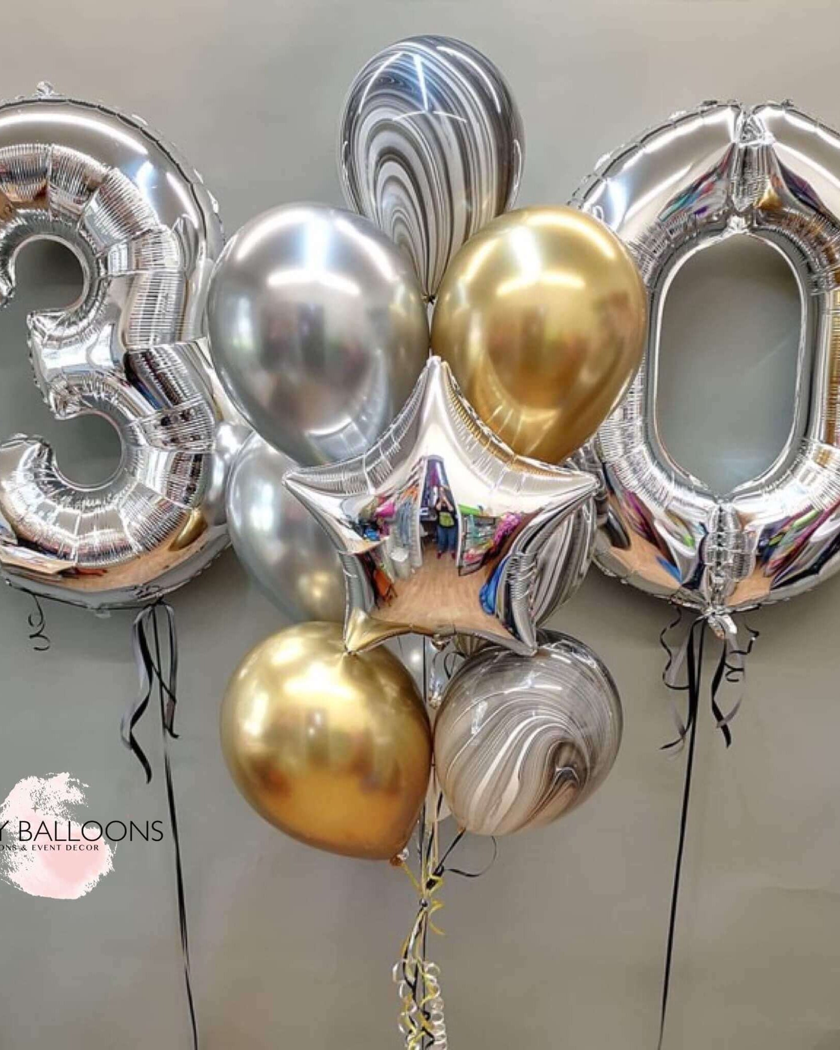 A bouquet of balloons arranged to form the number '30', featuring a mix of silver chrome and gold colors, with a silver star foil balloon included.