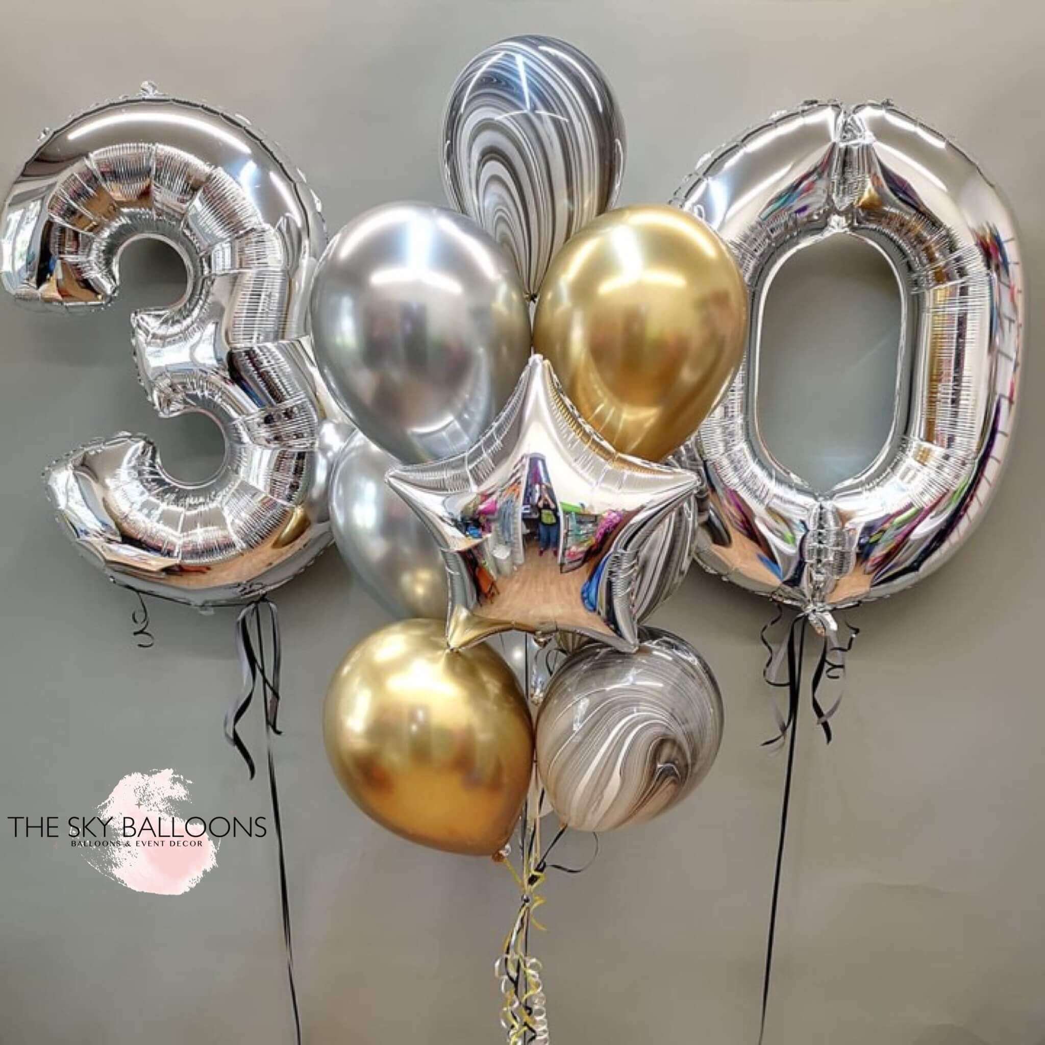 A bouquet of balloons arranged to form the number '30', featuring a mix of silver chrome and gold colors, with a silver star foil balloon included.