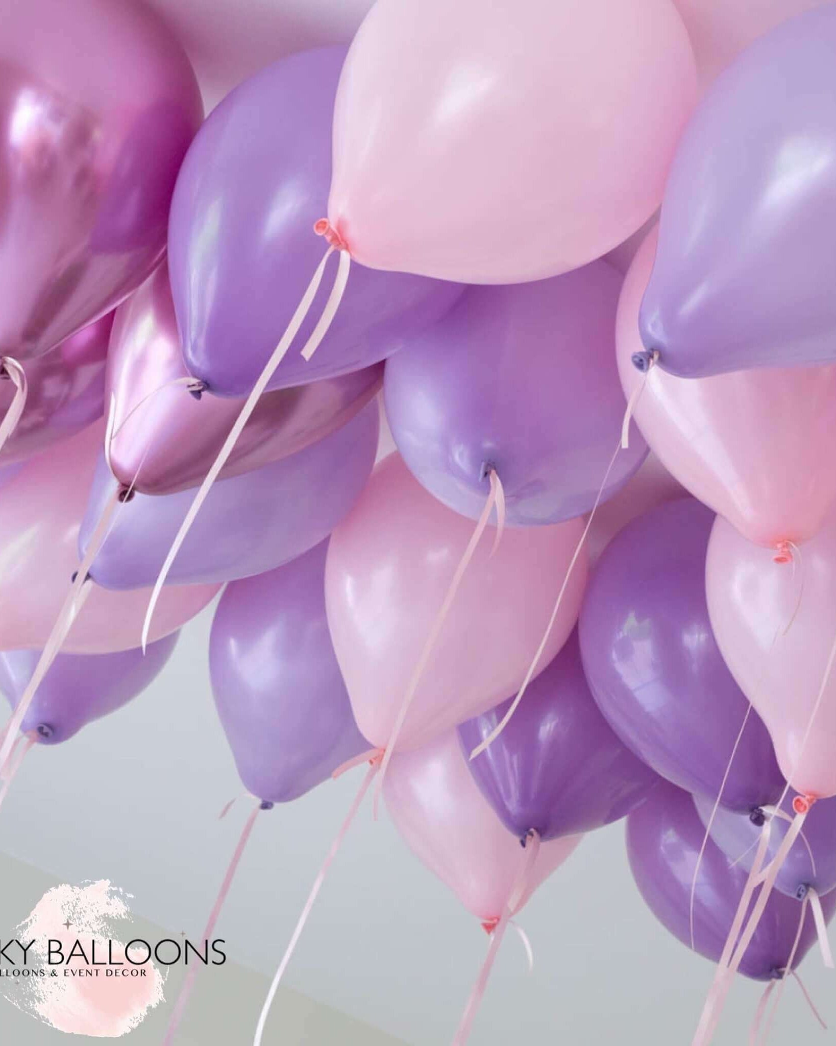 A cluster of inflated balloons in shades of purple, pink, and lavender, attached to strings, intended for ceiling decoration.