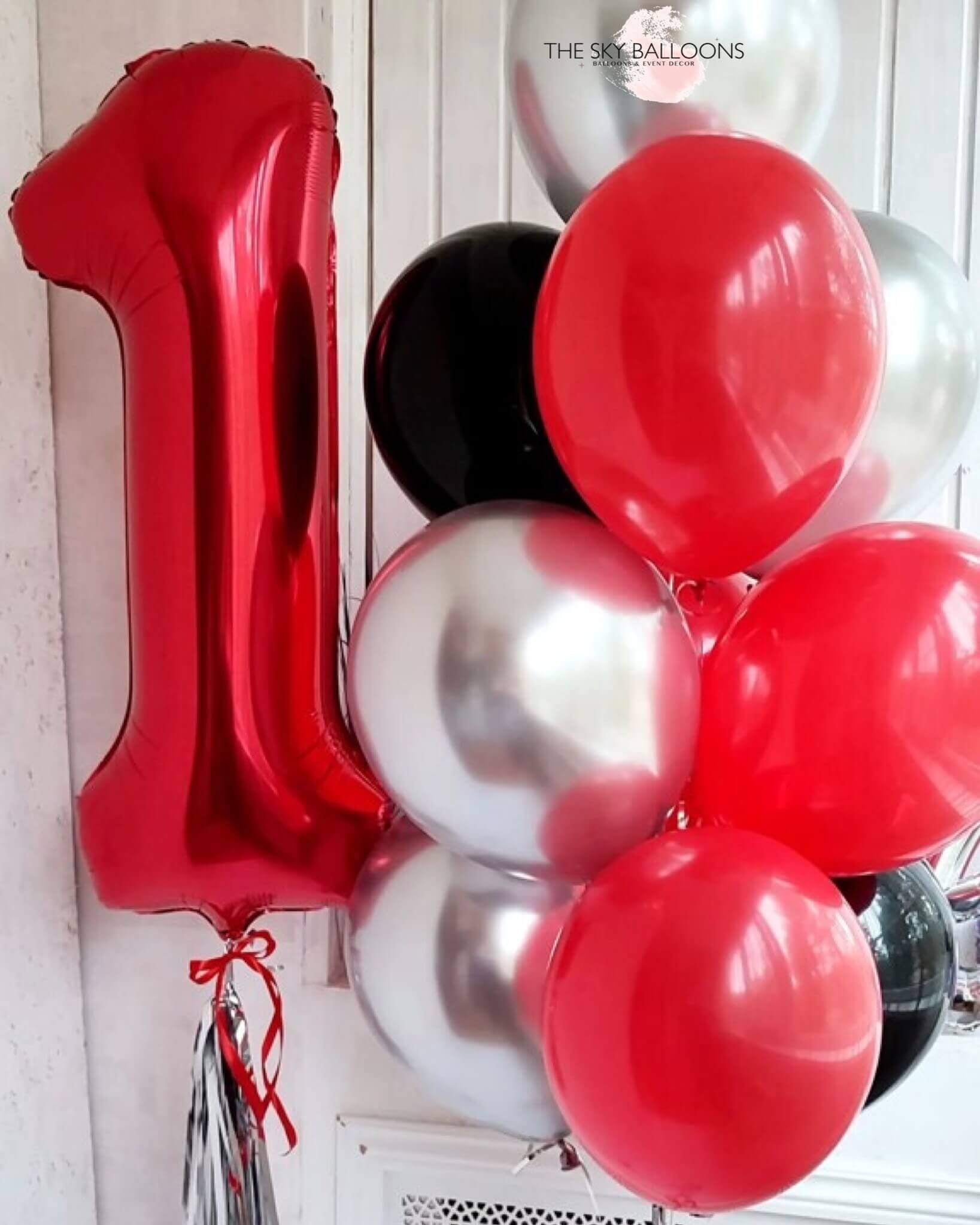 A bouquet of round latex balloons in red, silver, and black colors, with a large foil balloon in the shape of the number 1.
