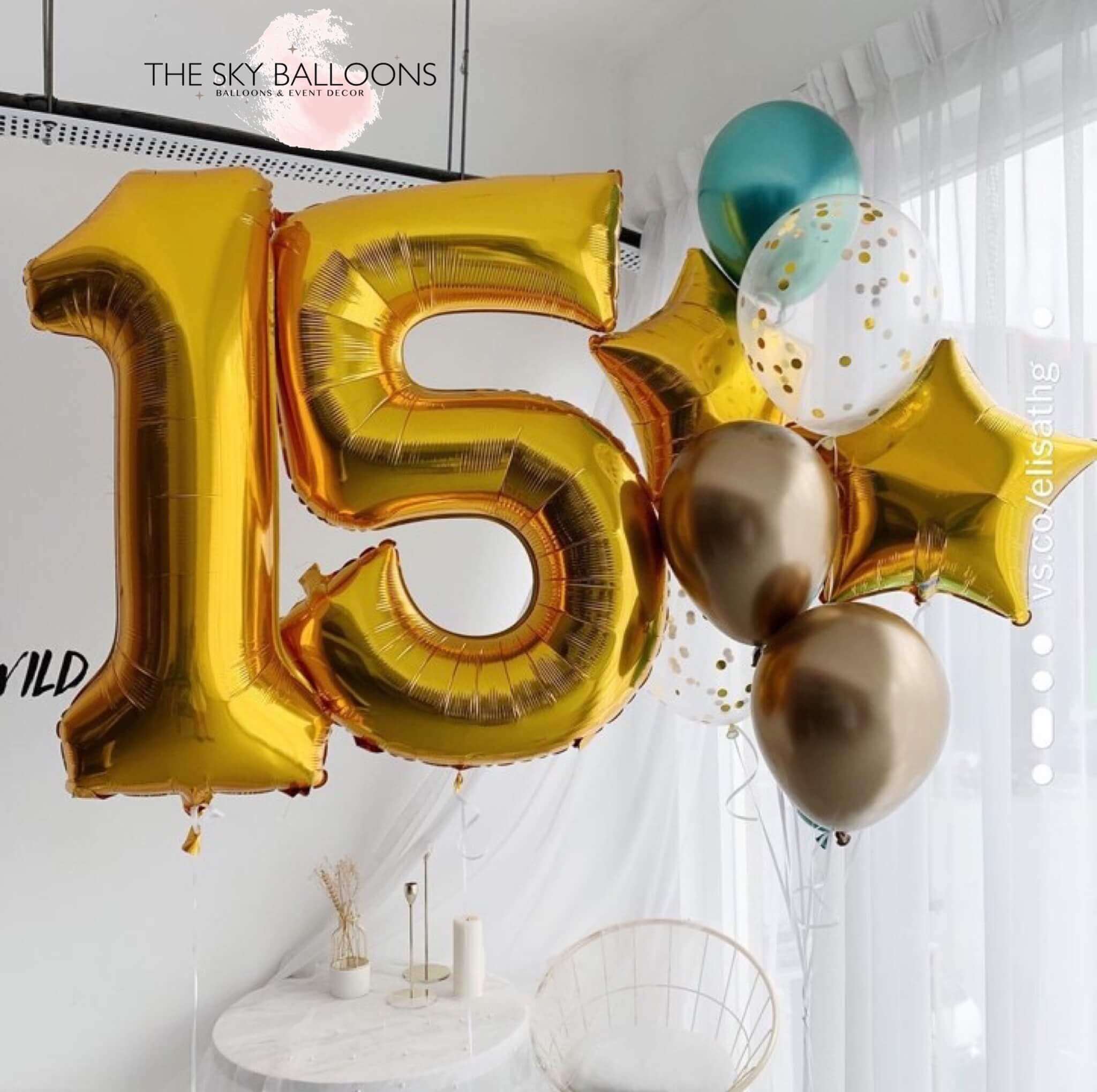 A set of inflated balloons displaying the number '15' in gold, with additional balloons in gold and silver colors, arranged indoors for a celebration.