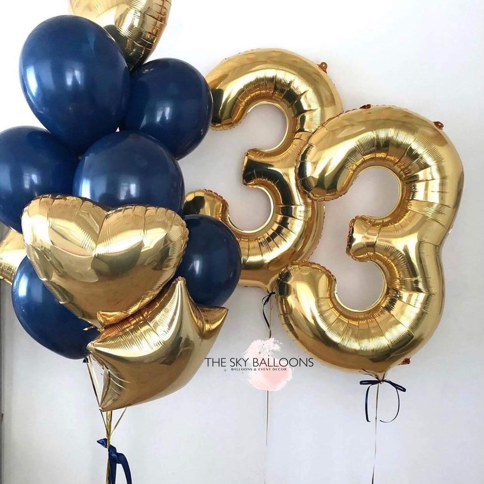 A bouquet of balloons including gold and navy blue colored latex balloons, with two gold star-shaped balloons, two gold heart-shaped balloons, and two gold numerical balloons spelling out a number.