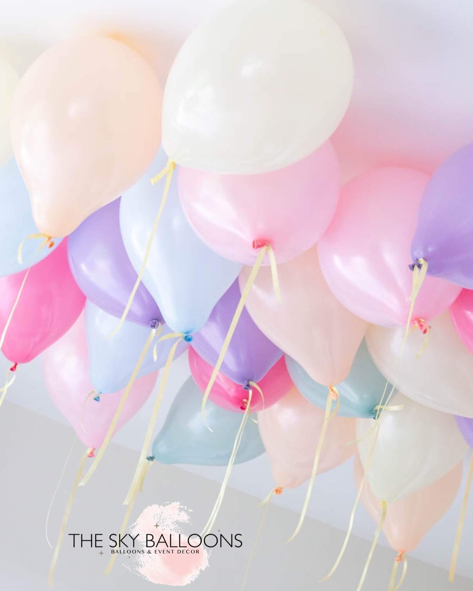 Inflated pastel rainbow colored latex balloons tied to strings and hanging from the ceiling, creating a festive decoration.