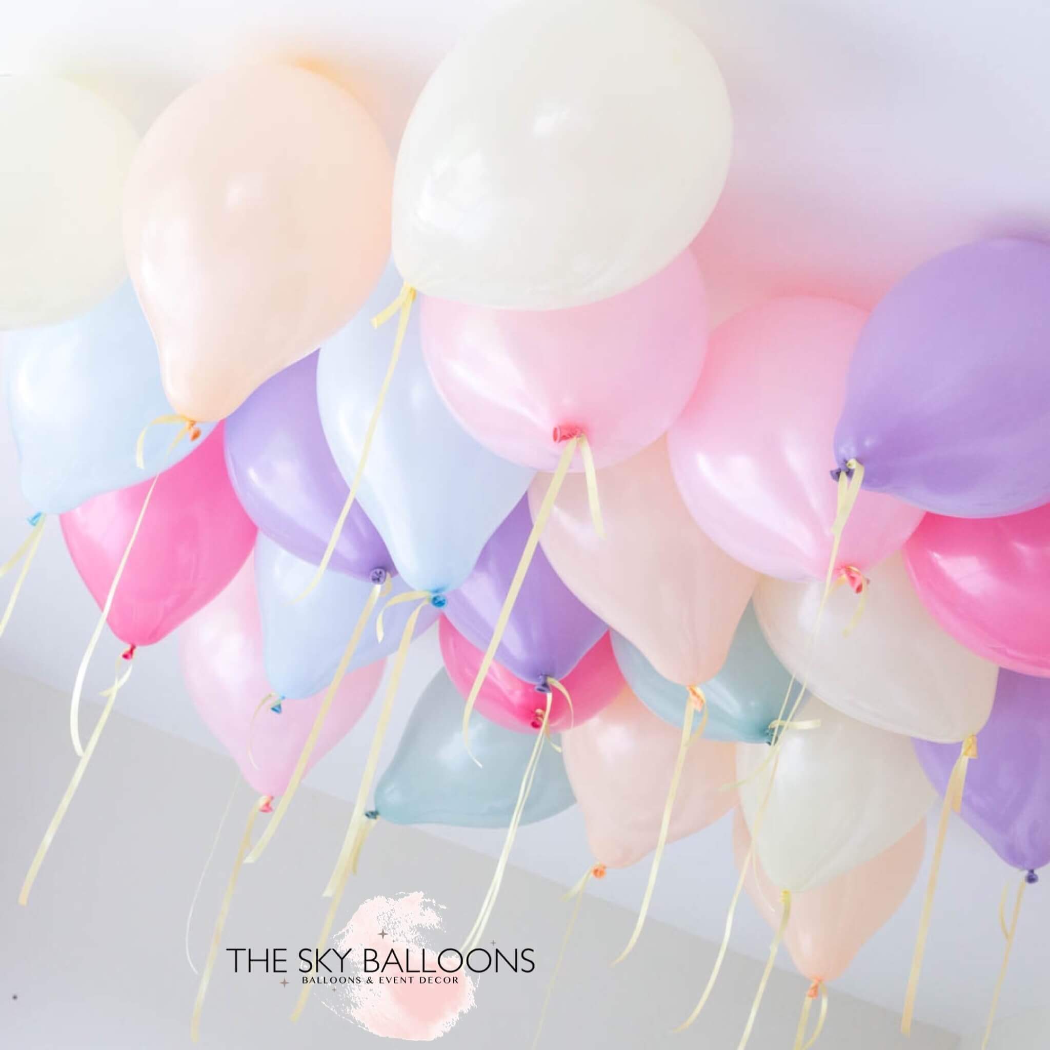 Inflated pastel rainbow colored latex balloons tied to strings and hanging from the ceiling, creating a festive decoration.