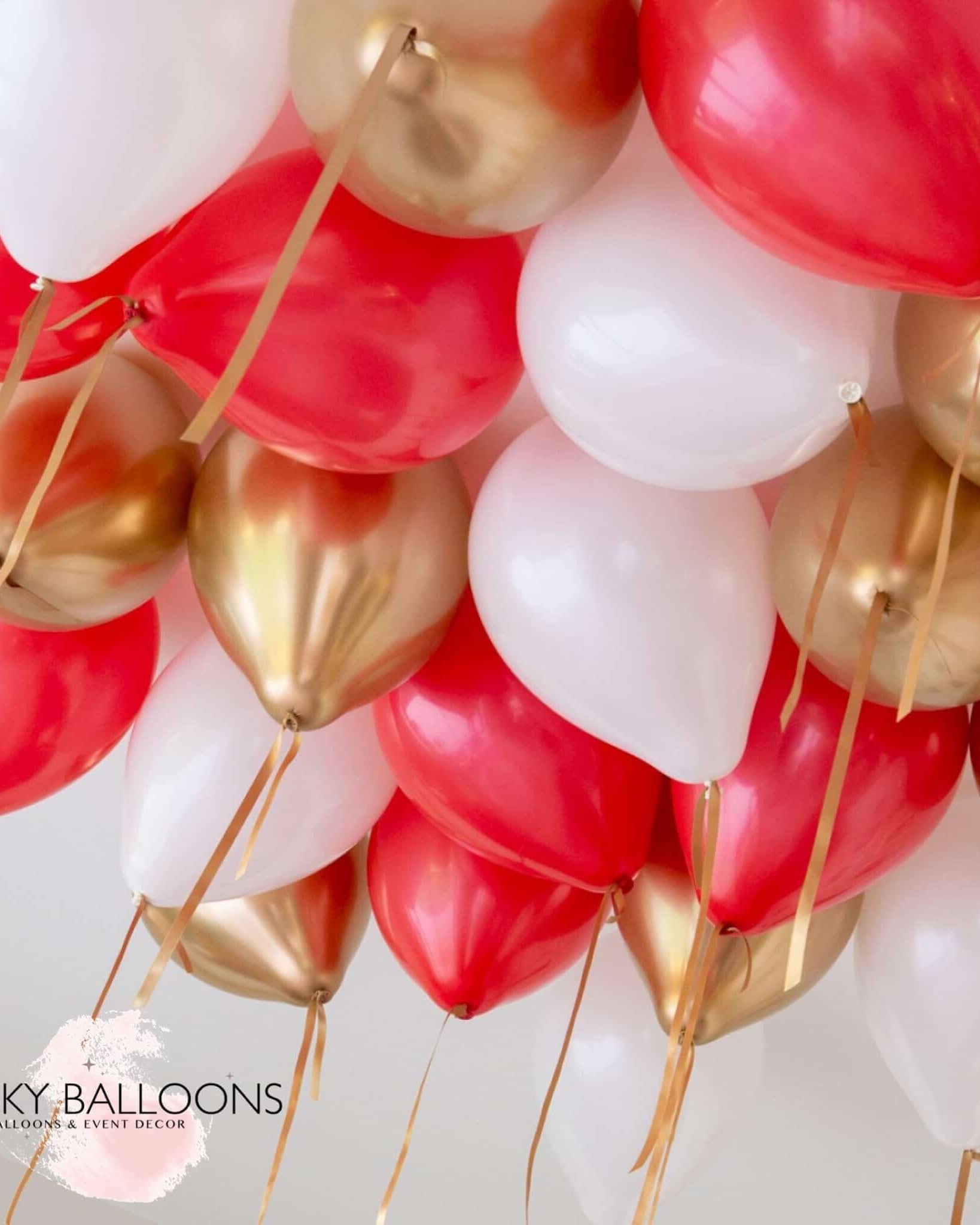 A cluster of inflated balloons in red, white, and gold colors, attached to strings, presumably intended for ceiling decoration.