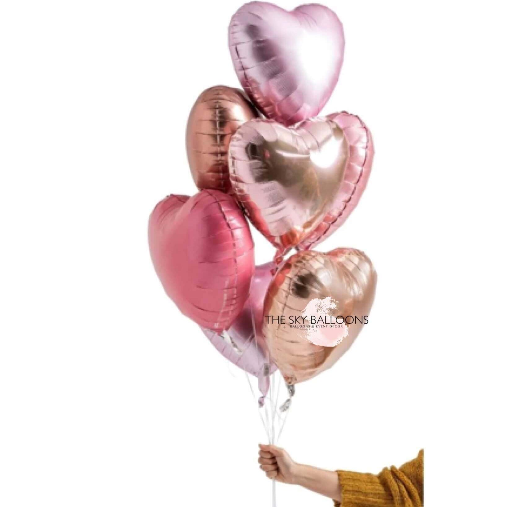A hand holding a bouquet of rose gold balloons with heart and star shapes, weighted down with helium.