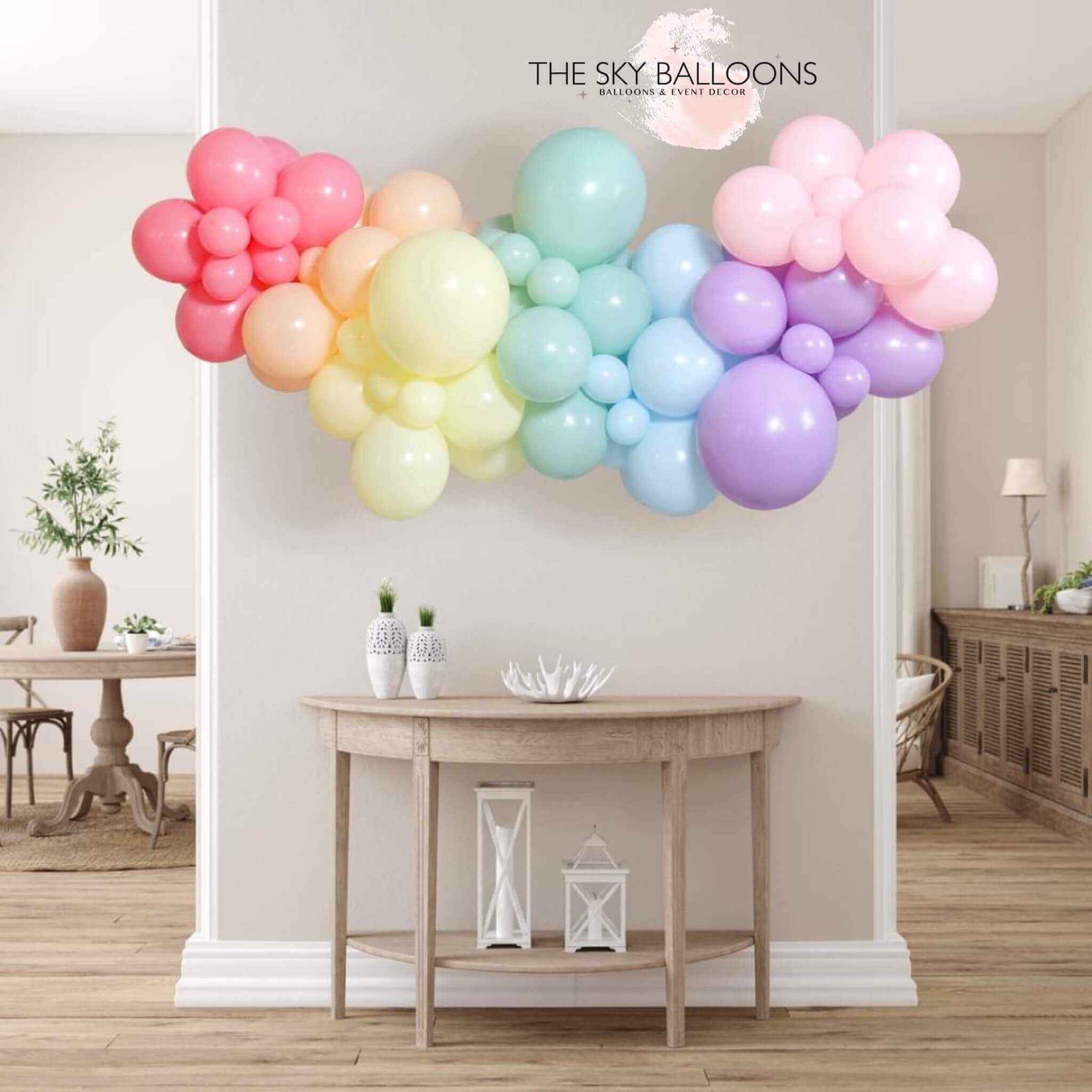 Colorful organic balloon garland decor by The Sky Balloons, featuring a mix of pastel-colored balloons arranged in a stylish, natural flow above a wooden console table in a modern living room setting.