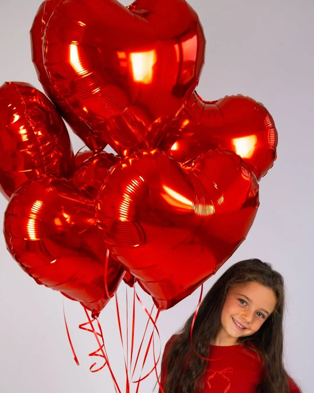 Girl holding red heart-shaped balloons against a plain background