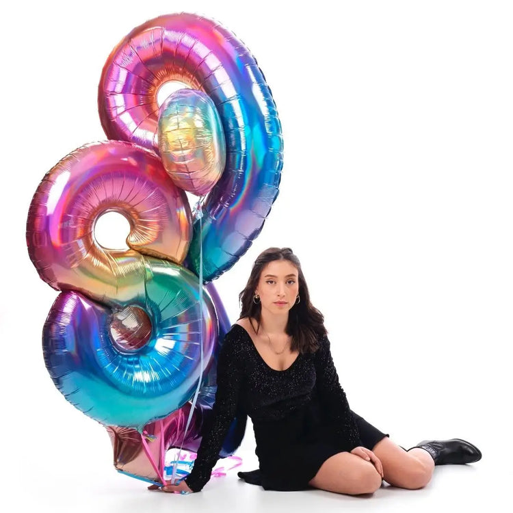 Woman sitting on the floor with large iridescent number balloons spelling '89' on a white background