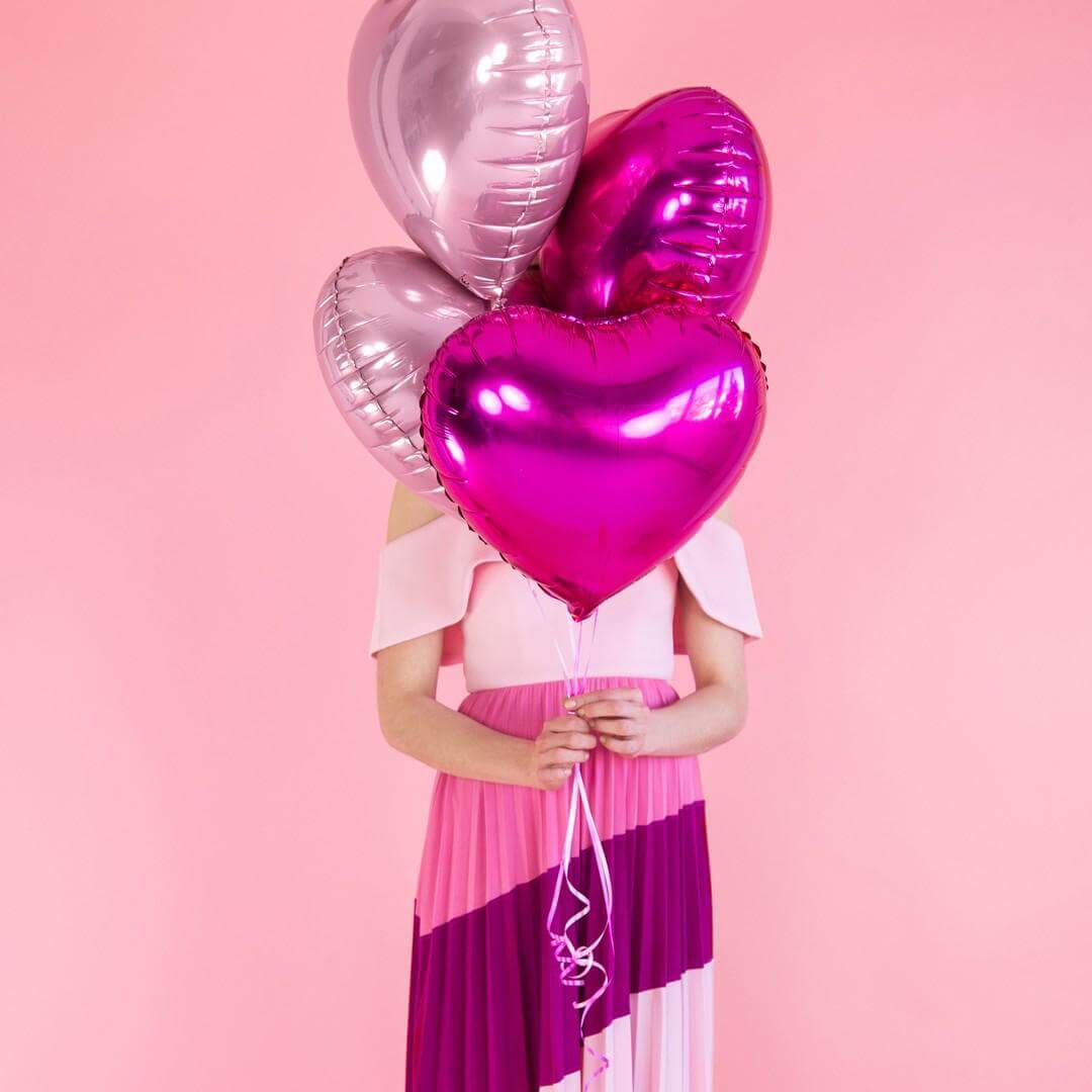 Girl holding red heart-shaped balloons against a plain background