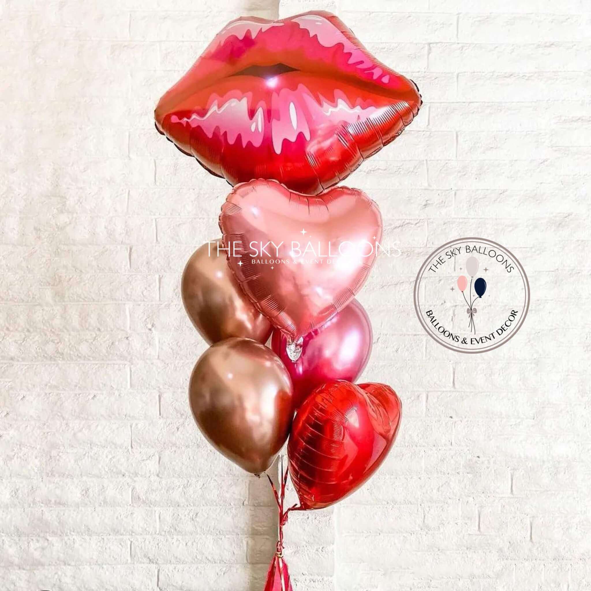 A balloon bouquet featuring a jumbo size lips balloon, heart-shaped balloons in pink and red, and other decorative balloons with the text 'Happy Valentine's' visible on one of the hearts.
