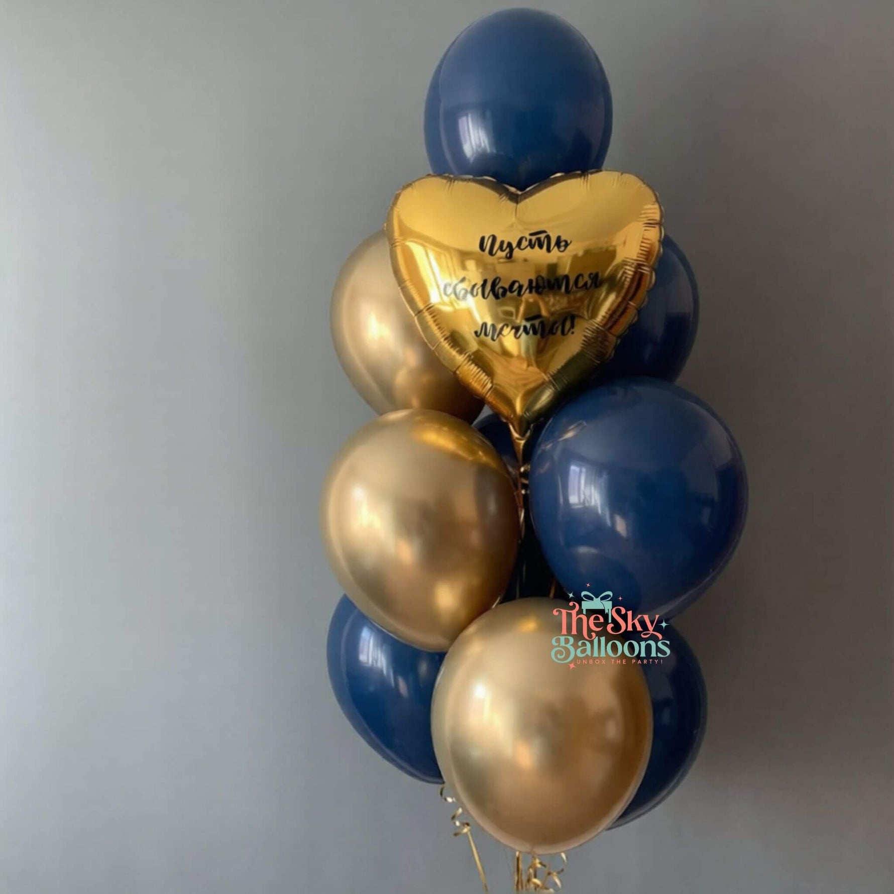 Balloon bouquet with blue and gold balloons, including a heart-shaped gold balloon with text, on a plain background.