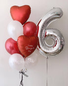  A colorful balloon bouquet featuring a large number six surrounded by red heart-shaped balloons.