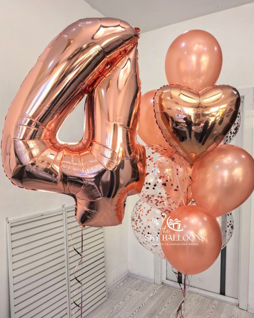 Rose gold foil balloon numbers, including a large '4' and smaller '1' and '5' balloons, displayed with clear balloons containing rose gold confetti in an indoor setting.