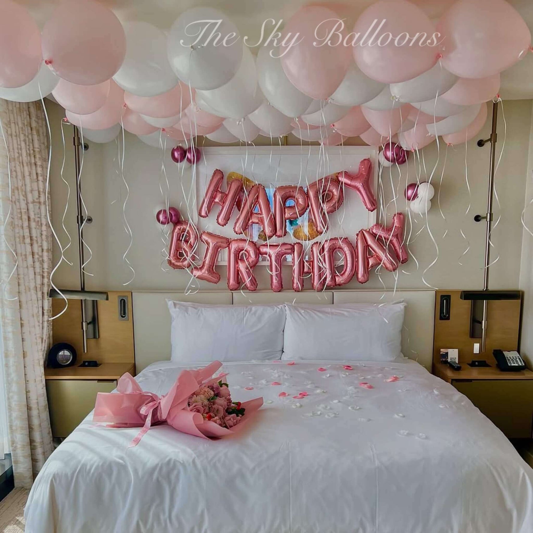 Bedroom decorated with pink and white balloons, 'Happy Birthday' sign, and flowers.