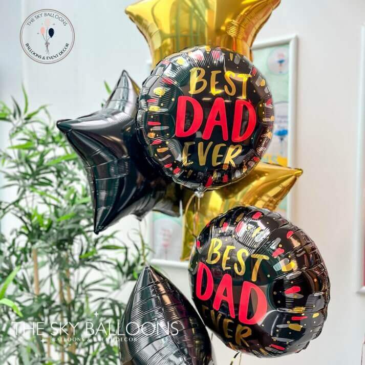 A set of helium-filled balloons, with two larger round balloons reading 'BEST DAD EVER' in red and black, and four star-shaped balloons in gold and black. All balloons are inflated and arranged together.