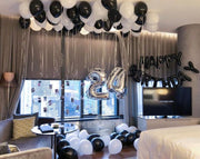 A festive room with colorful balloons and a bed adorned with a birthday sign.