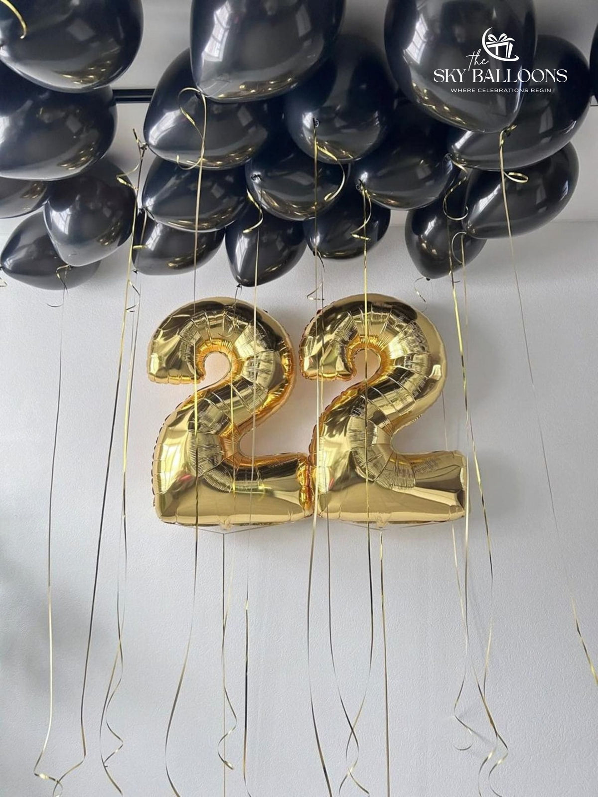 Black ceiling balloons with hanging gold ribbons and gold number 22 foil balloons on the wall.