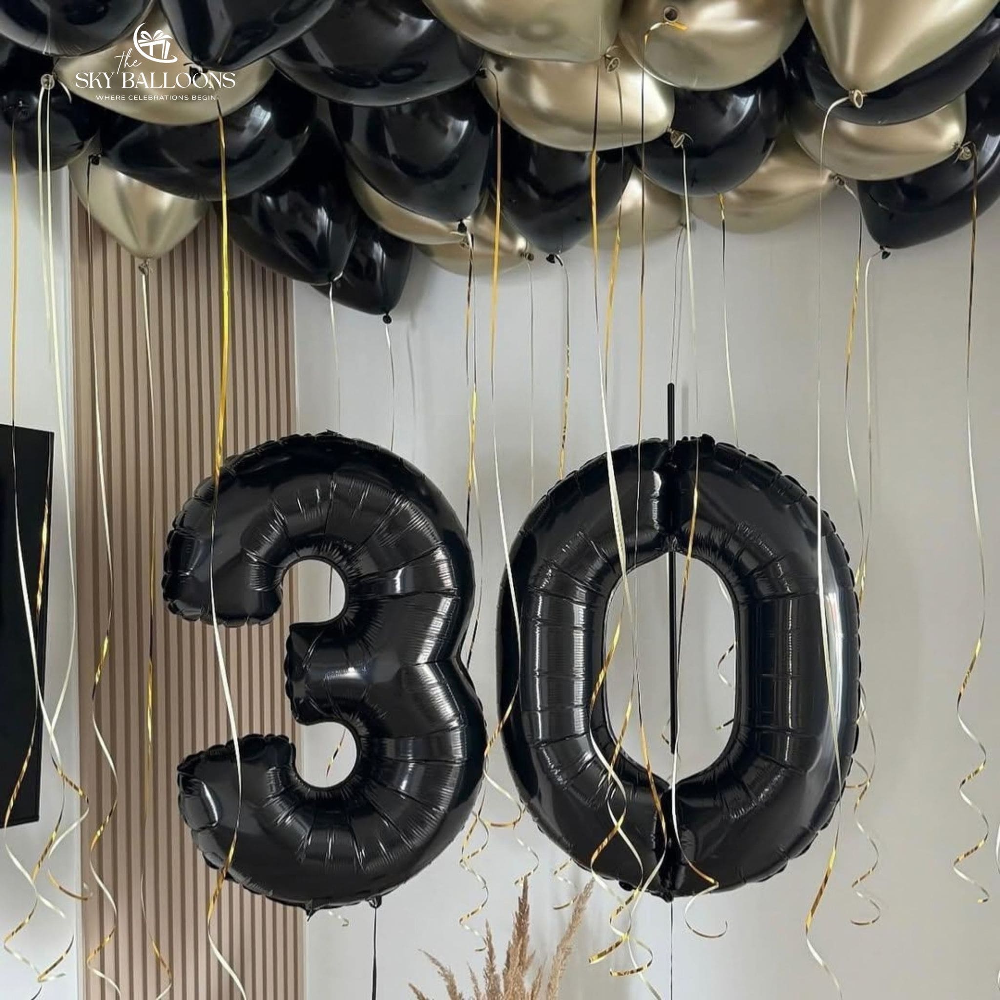 Black number 30 foil balloons beneath black and chrome-gold ceiling balloons with hanging ribbons.