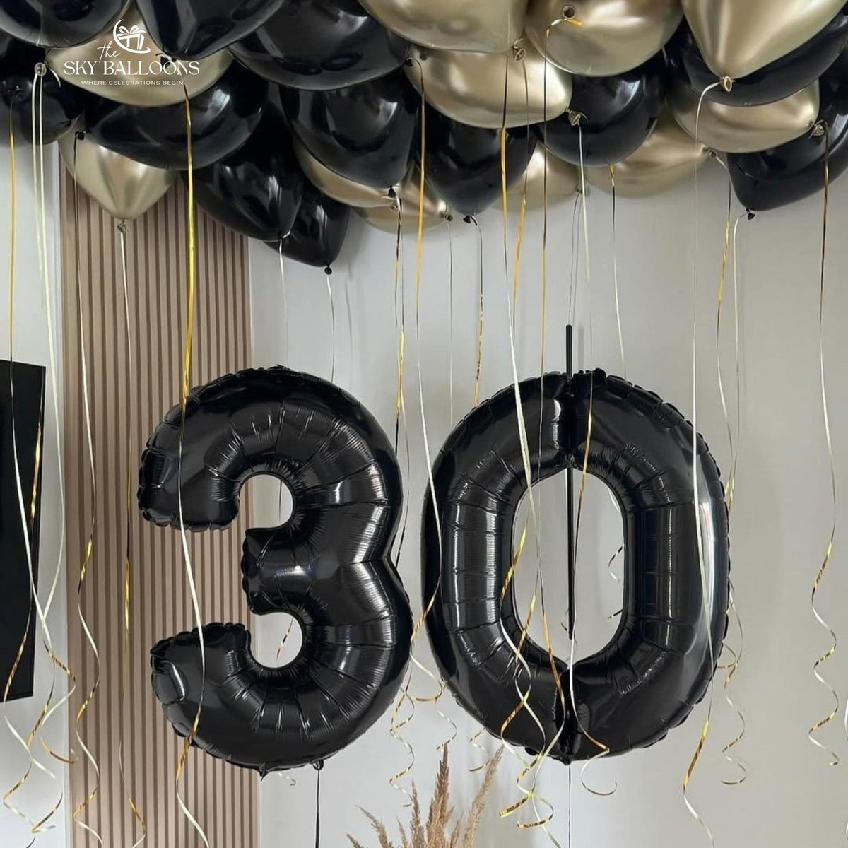 Black number 30 foil balloons beneath black and chrome-gold ceiling balloons with hanging ribbons.