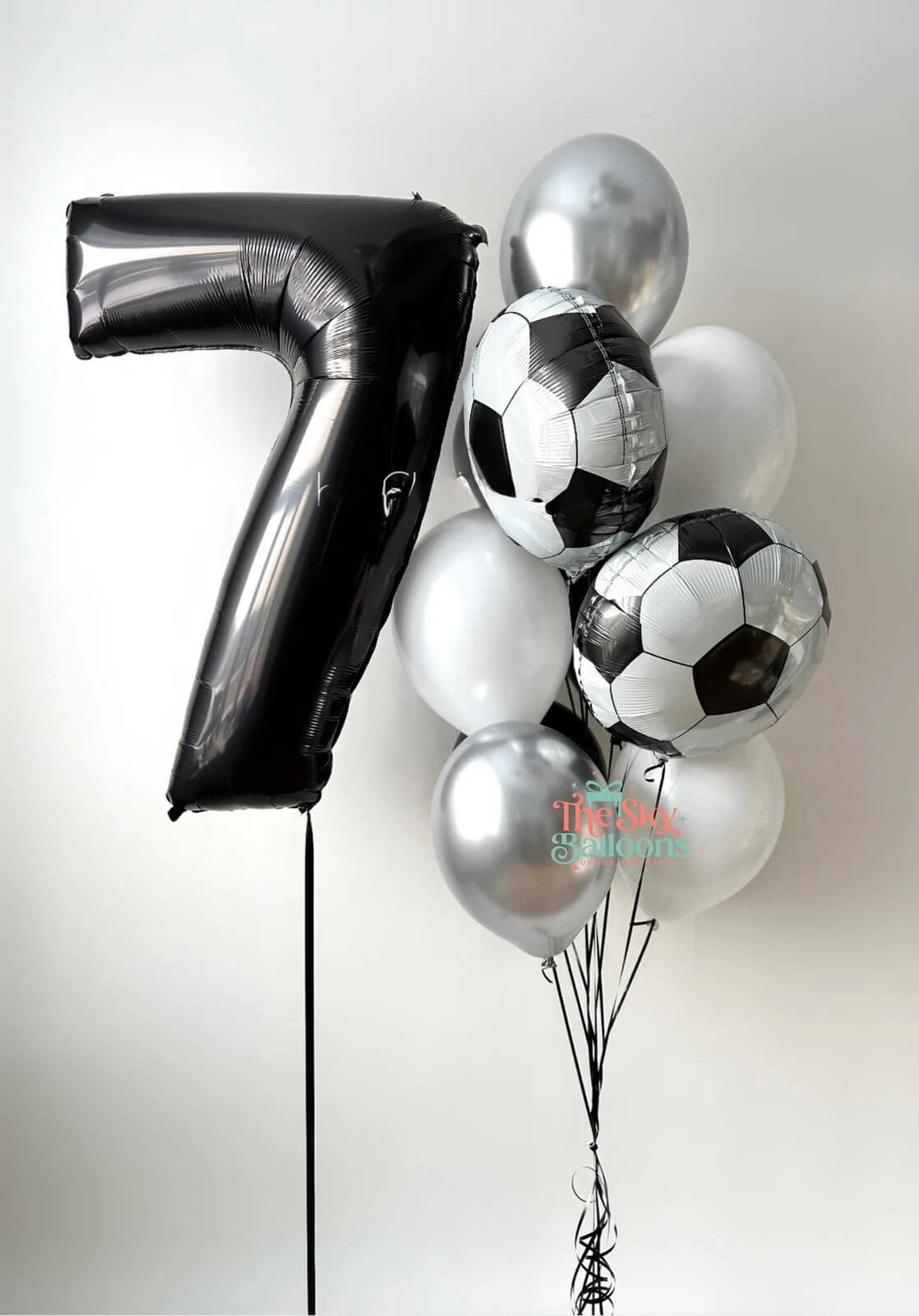 Bouquet of balloons including a large number 7, soccer ball-shaped balloons, and silver balloons on a white background.