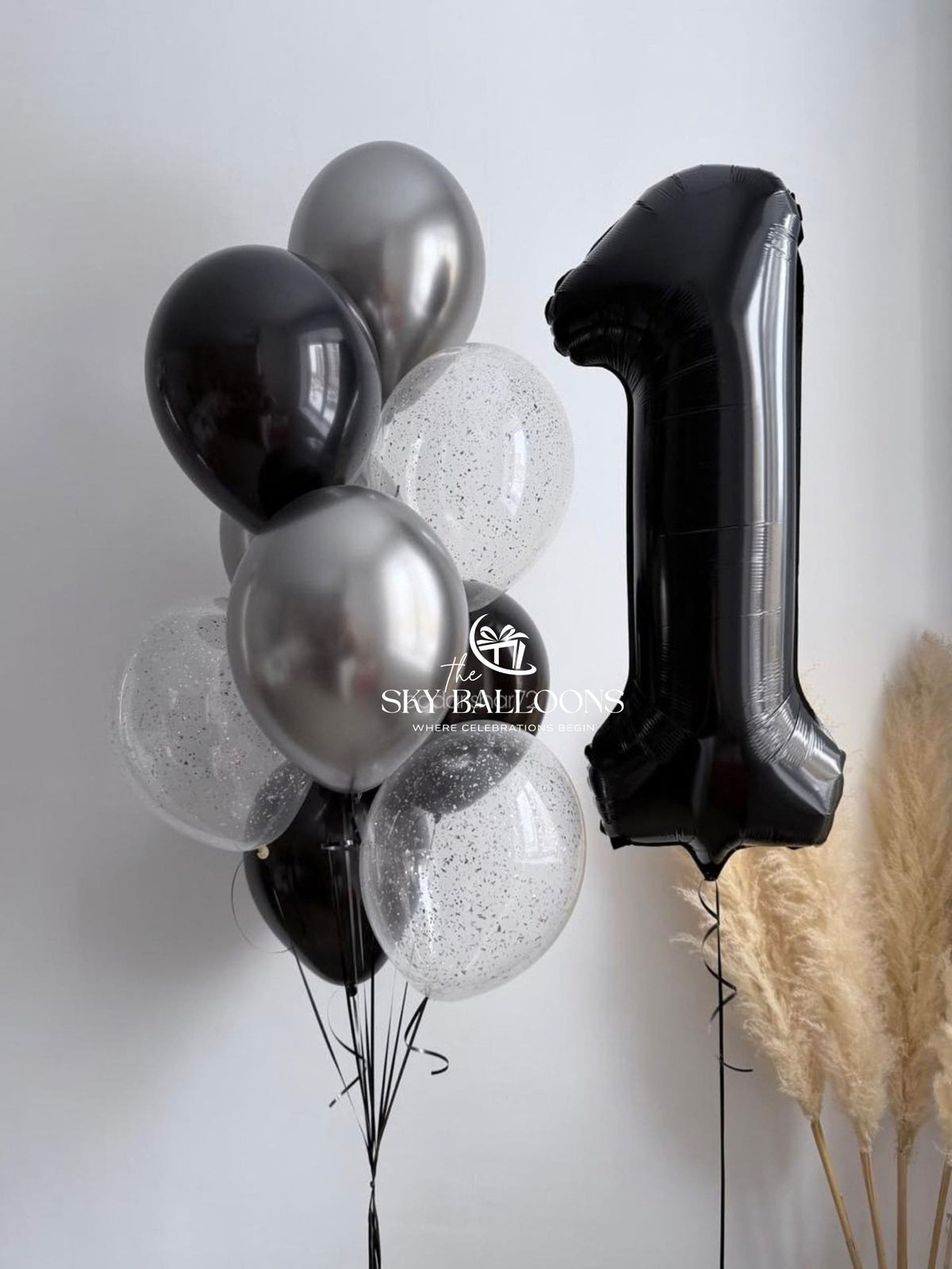 Black number 1 foil balloon beside a bunch of black, chrome-silver and clear silver-confetti latex balloons.