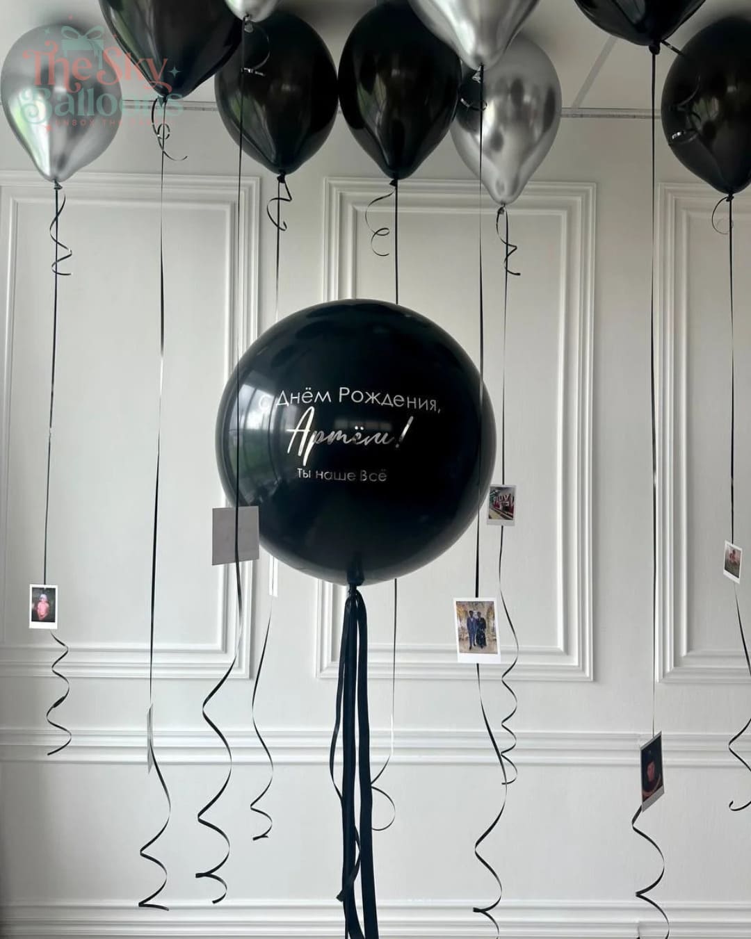 Black balloons with text hanging against a white paneled wall.