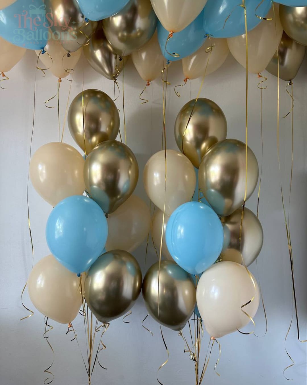 Balloons in gold, blue, and beige colors hanging against a light gray background.
