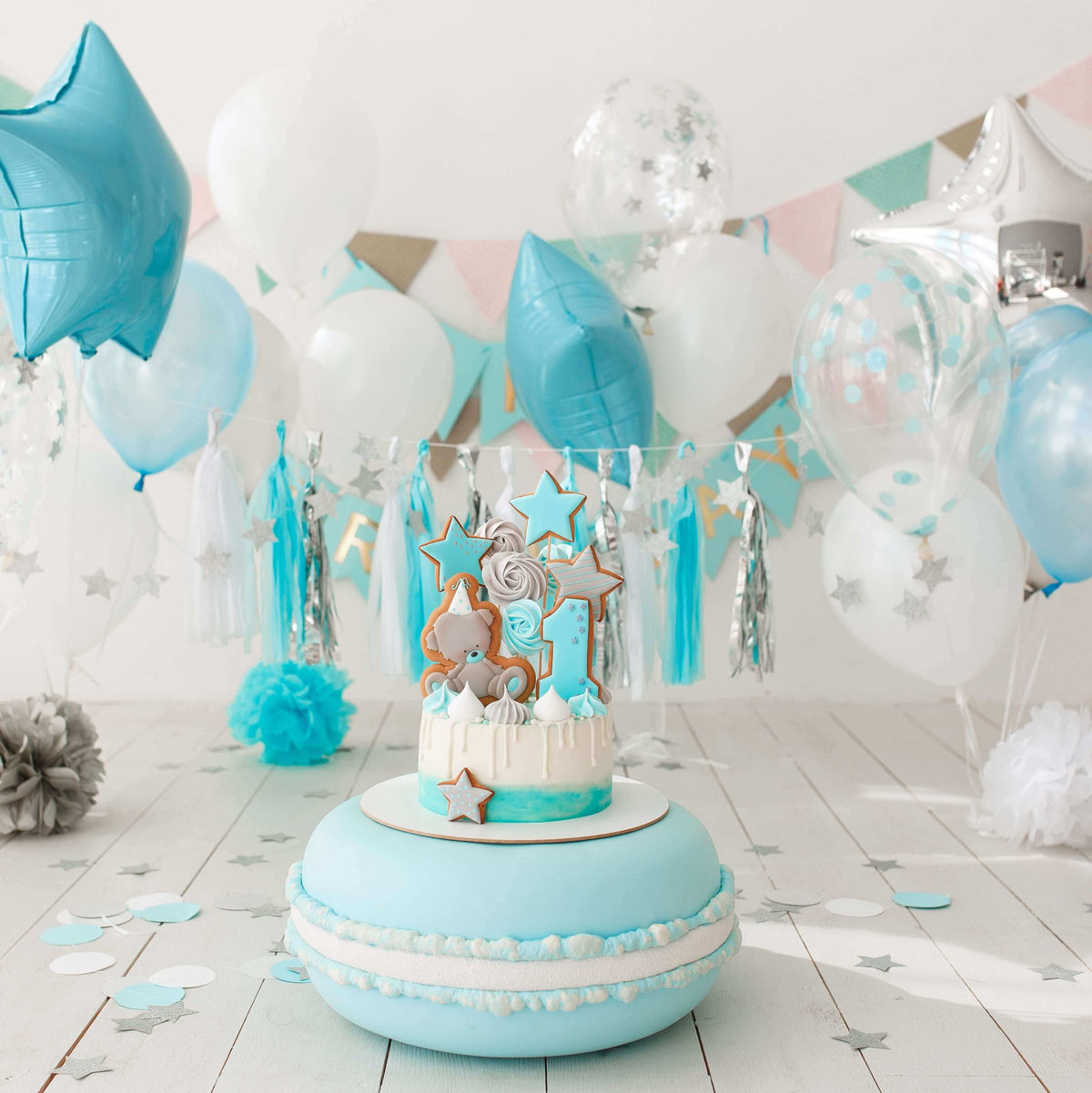 Blue and white first birthday setup with star-shaped balloons, a decorated cake, and festive garlands.