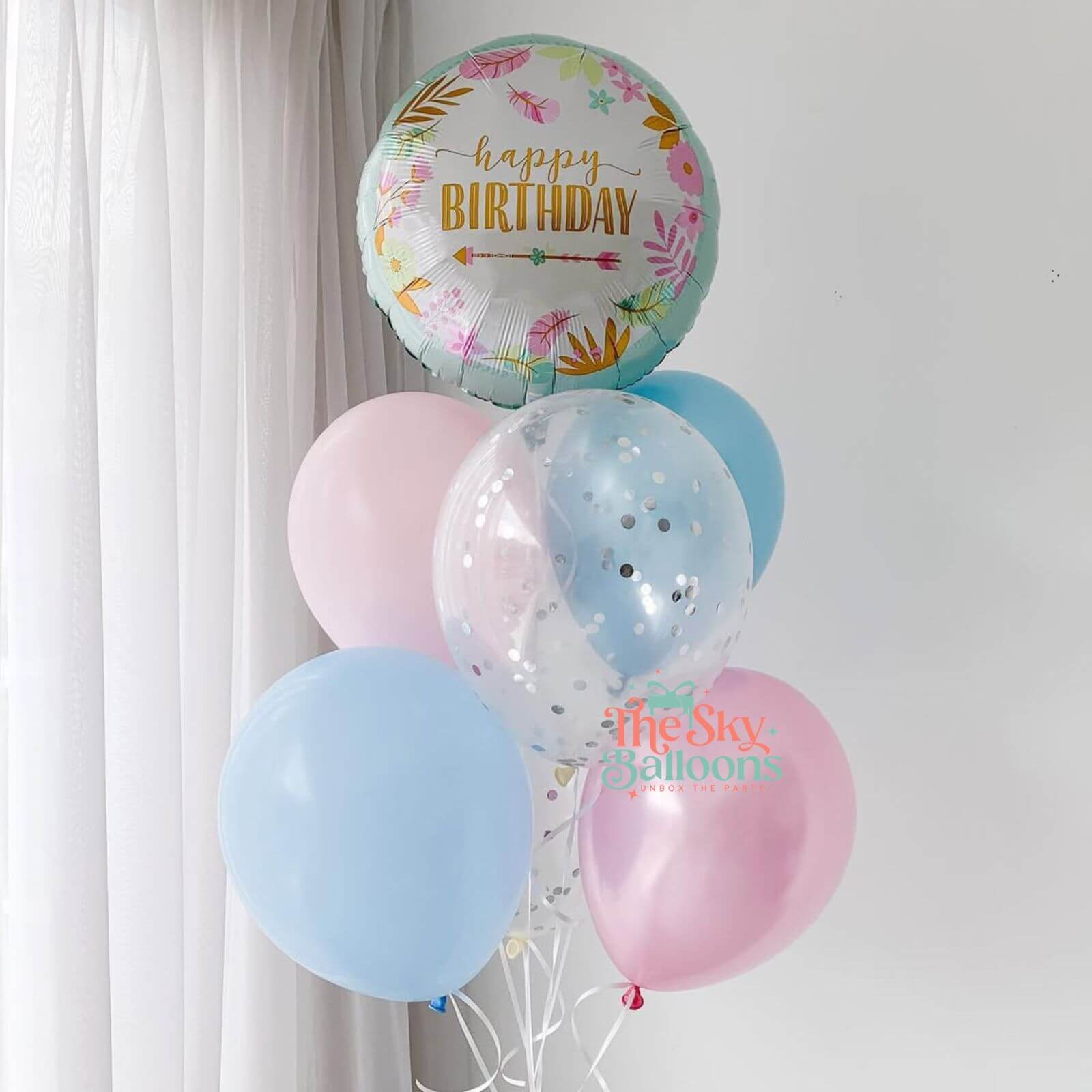 Bouquet of pastel balloons with a 'Happy Birthday' balloon against a white curtain background.
